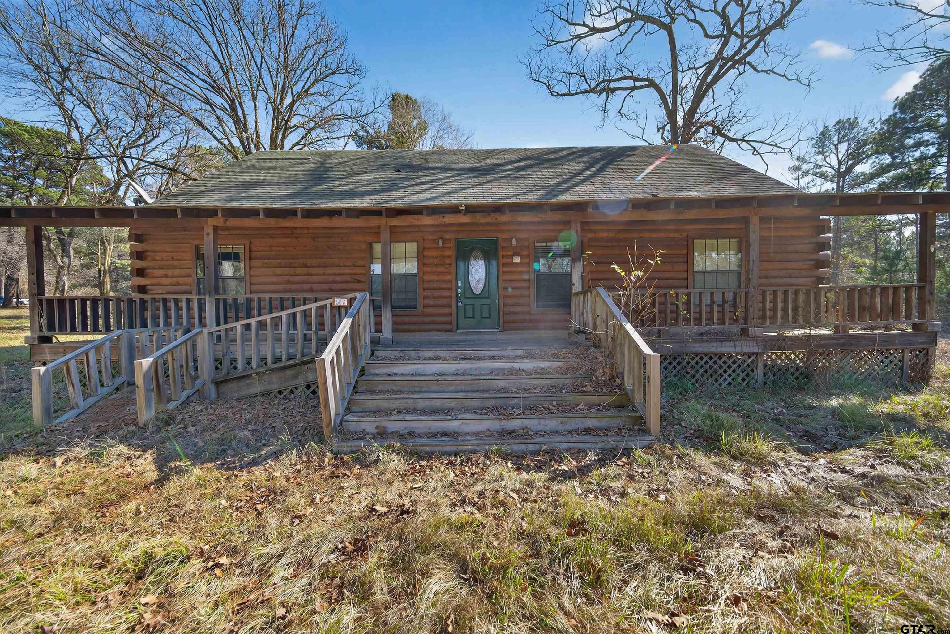 Log cabin front with a covered porch, wooden steps, and an accessibility ramp.