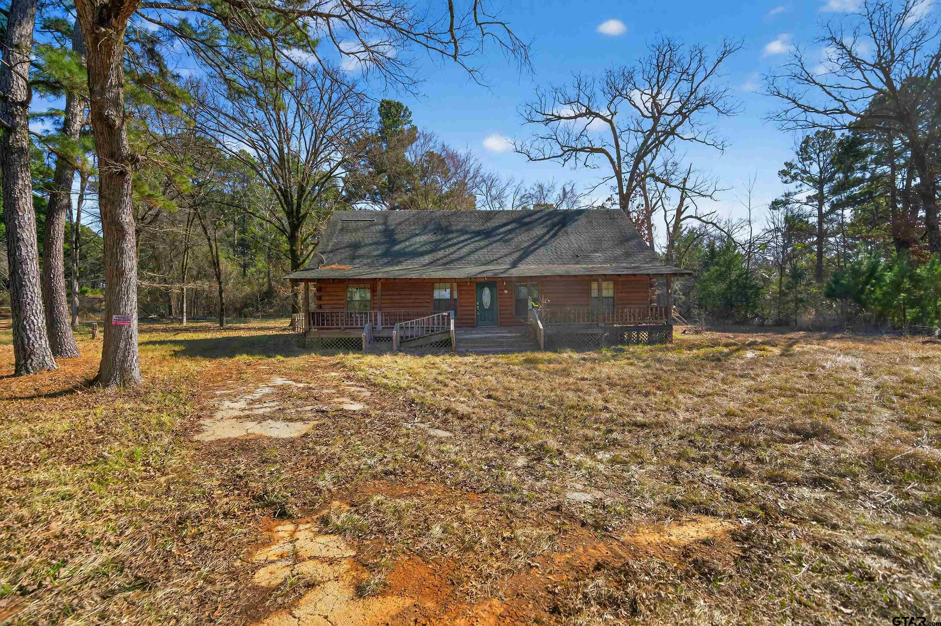 Log-sided house with a covered porch among mature trees, viewed from the front yard.