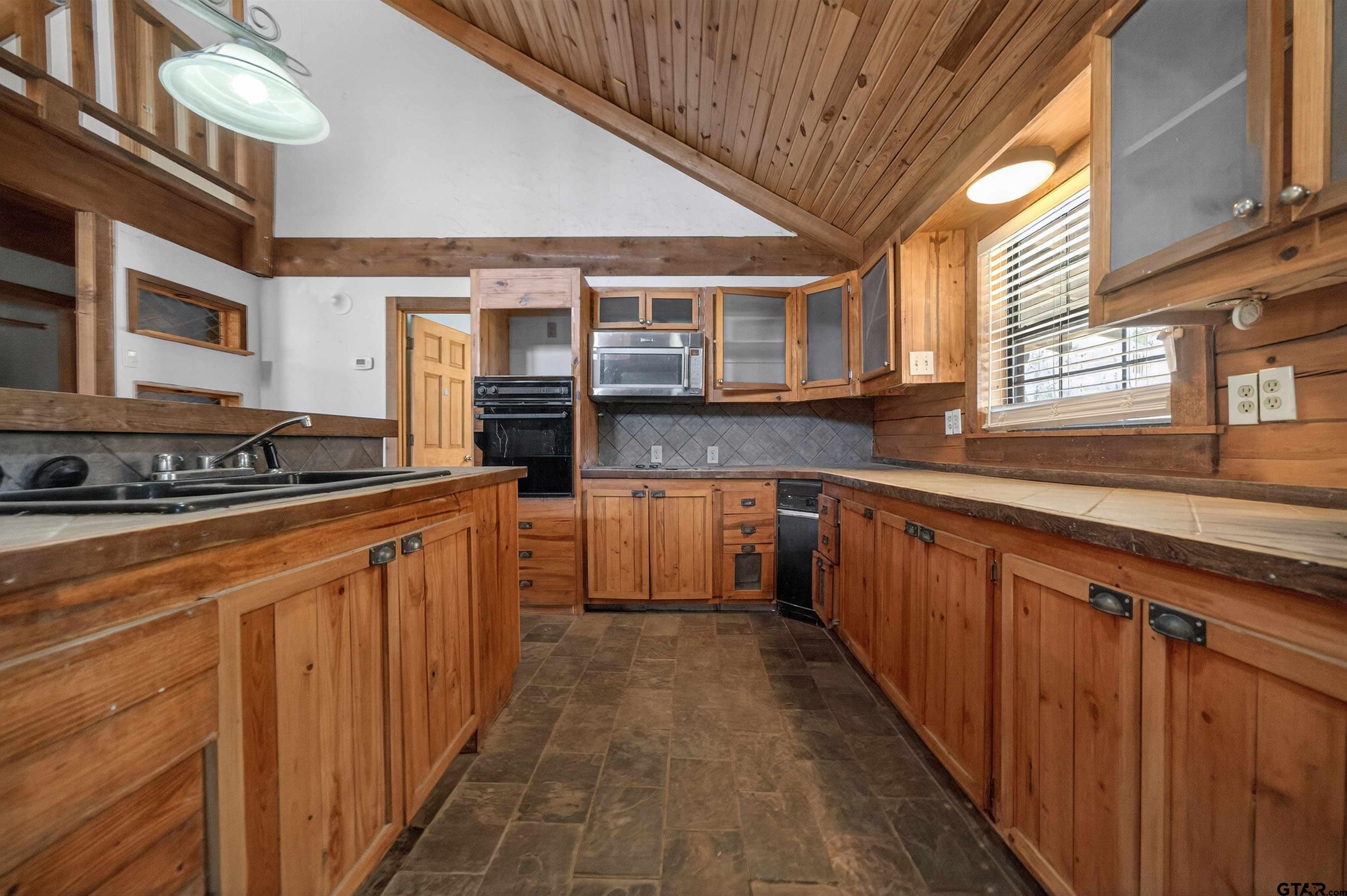 Kitchen with wood cabinetry, a vaulted wood ceiling, and a central sink island.