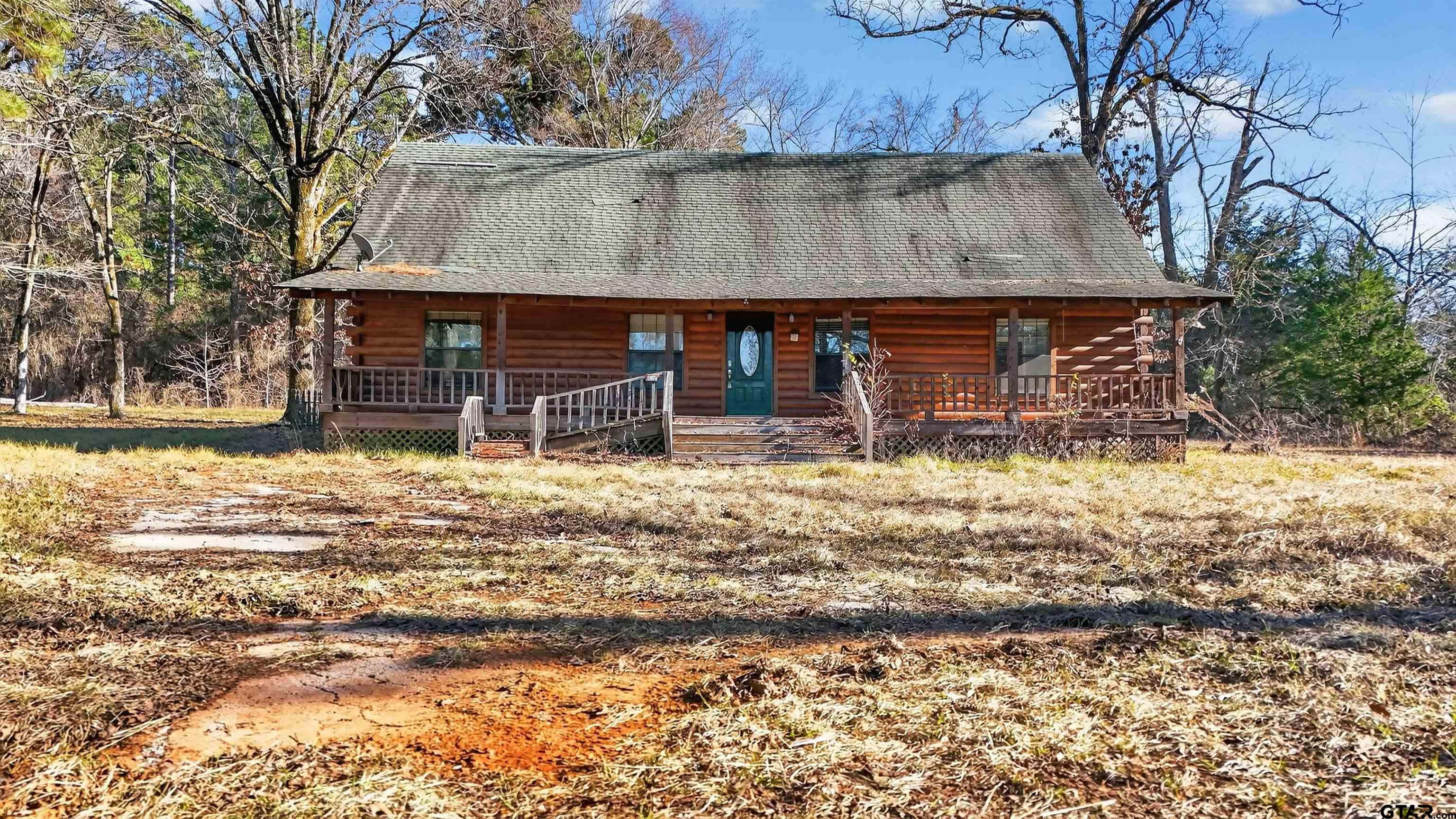Log cabin with a broad covered porch and teal front door among leafless trees.
