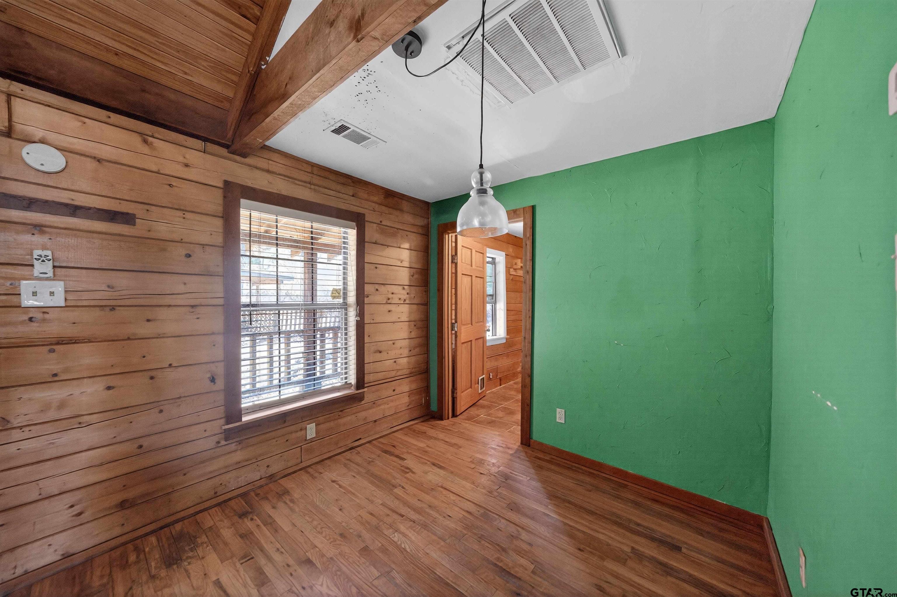Vacant room with hardwood floors, wood-plank walls, and a green accent wall.