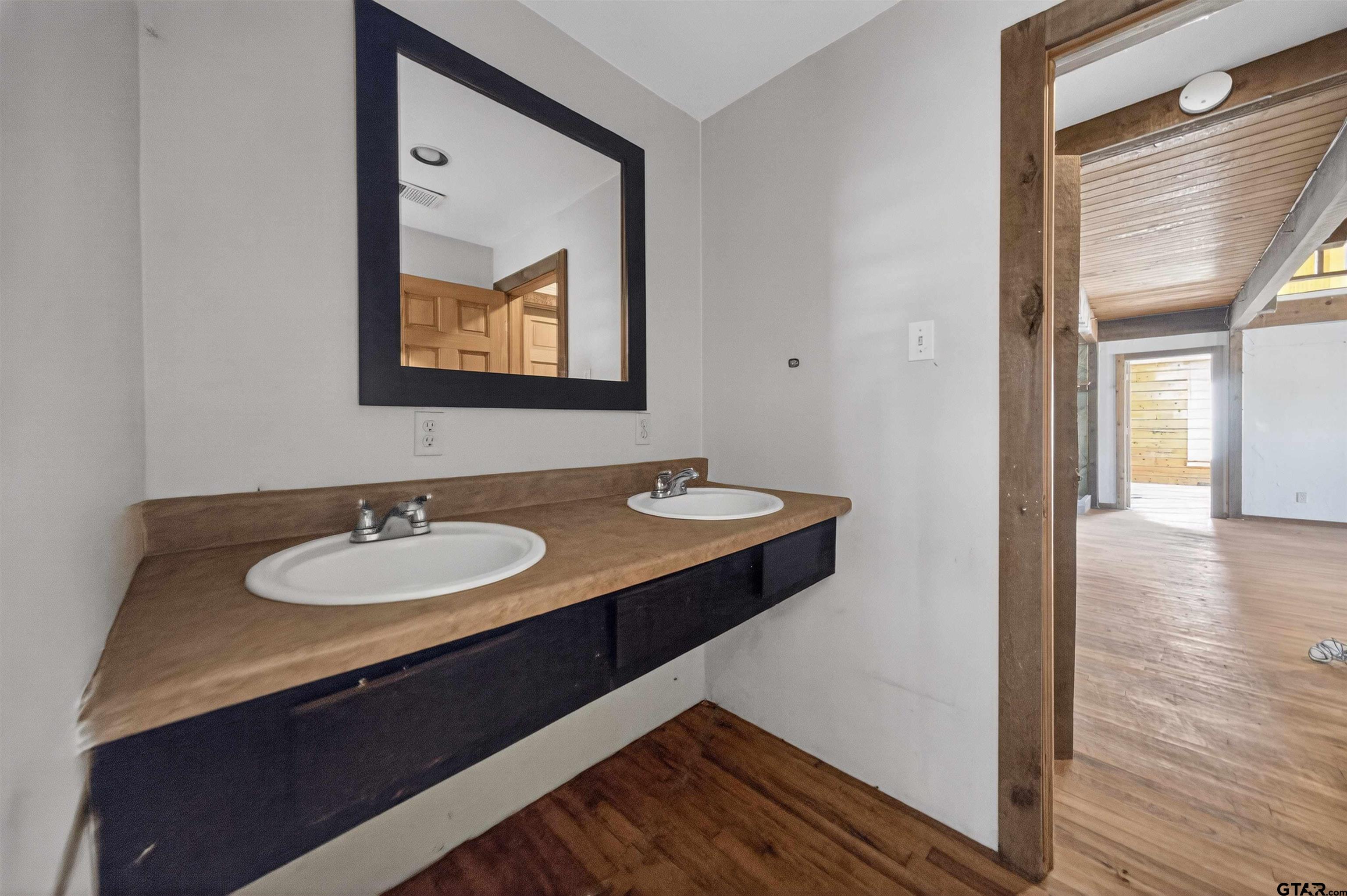 Bathroom with a double-sink vanity, wood-look countertop, and large framed mirror.