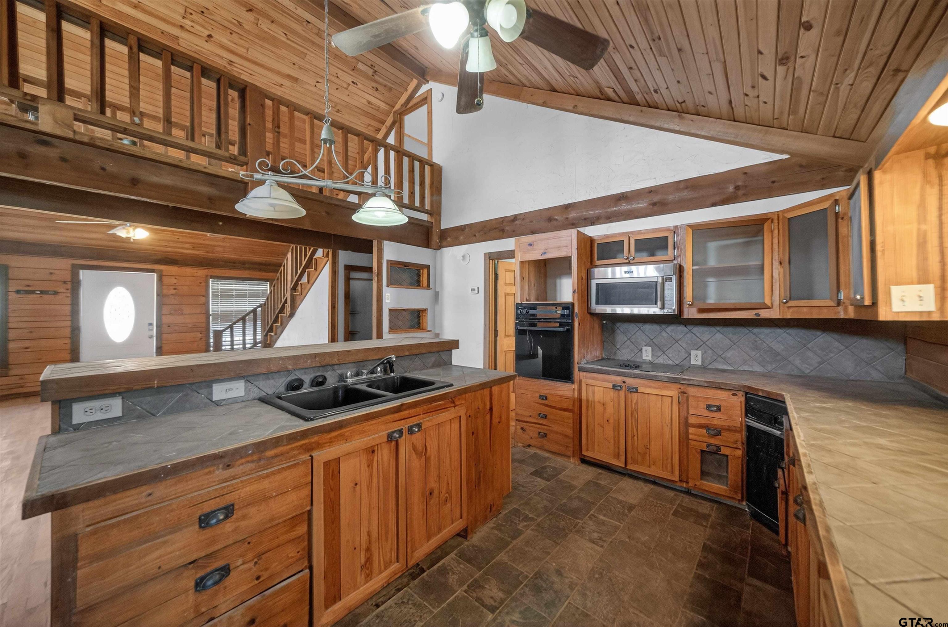 Kitchen with warm wood cabinetry, gray tile counters, and a vaulted ceiling with an open loft.