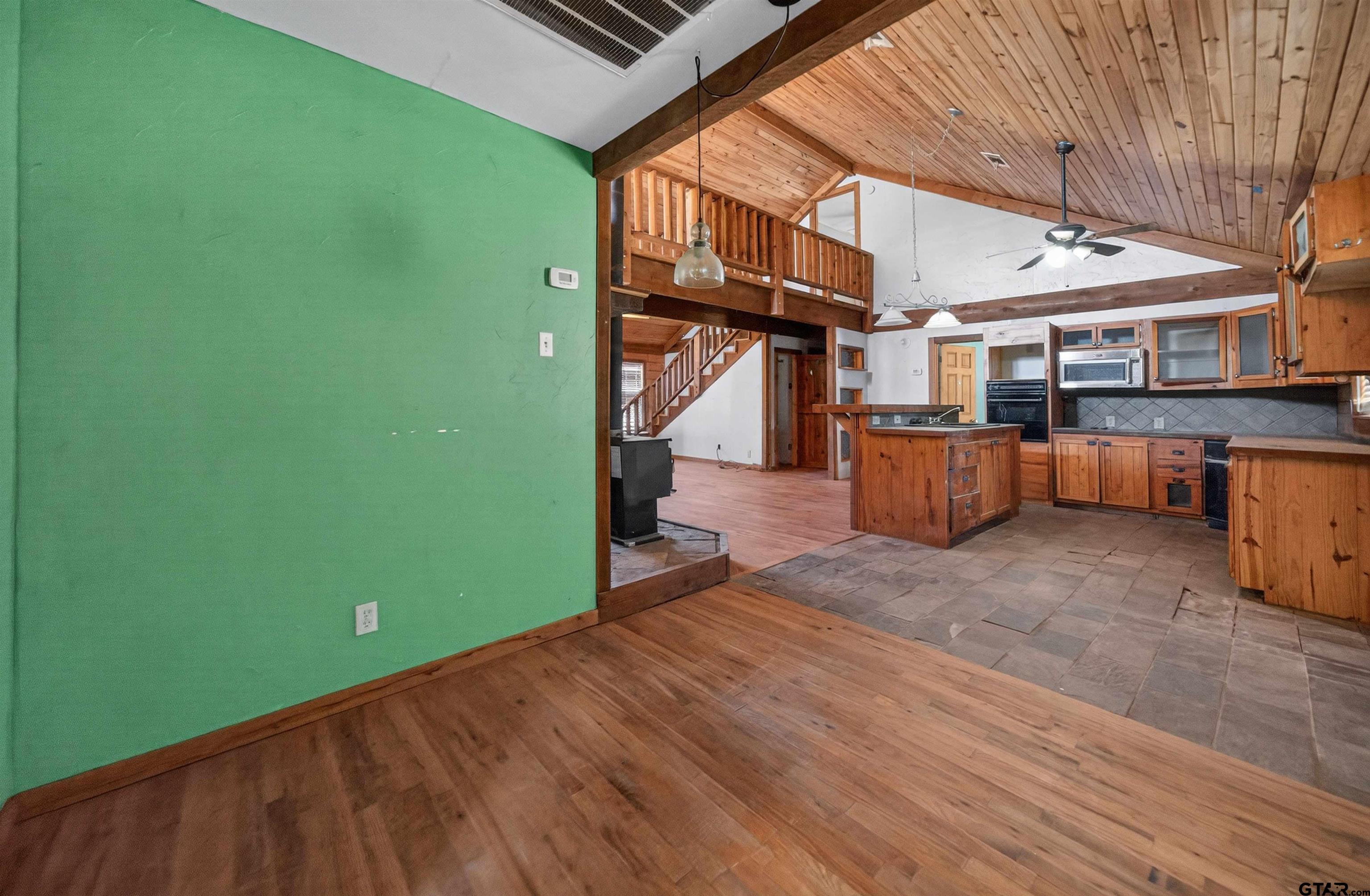 Open-plan kitchen with a wood-paneled vaulted ceiling, central island, and staircase to a loft.