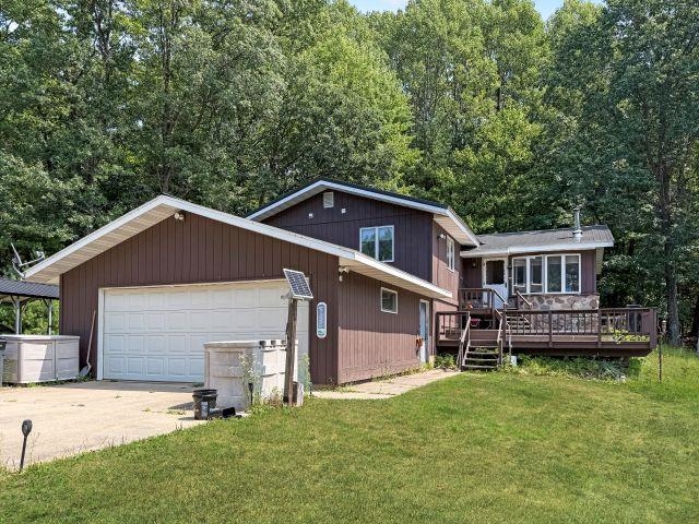 Brown house with an attached garage and raised deck, surrounded by lawn and trees.
