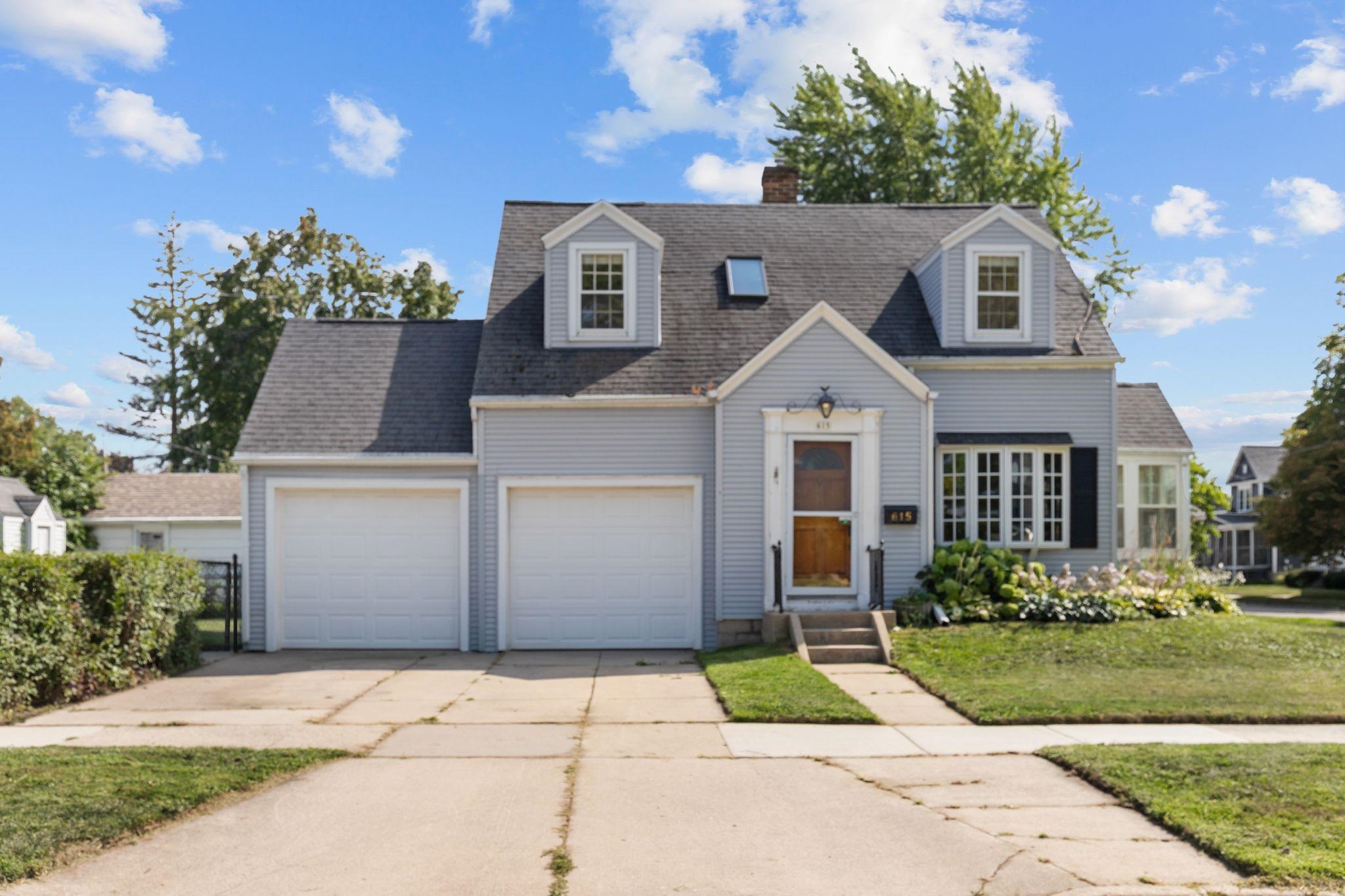 Gray two-story house with two garage doors, dormer windows, and a landscaped front lawn.