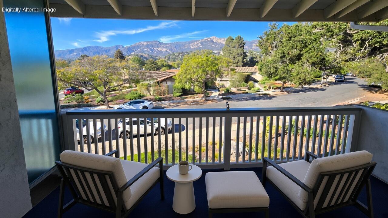 Covered balcony with cushioned seating overlooks a residential street and mountain range.