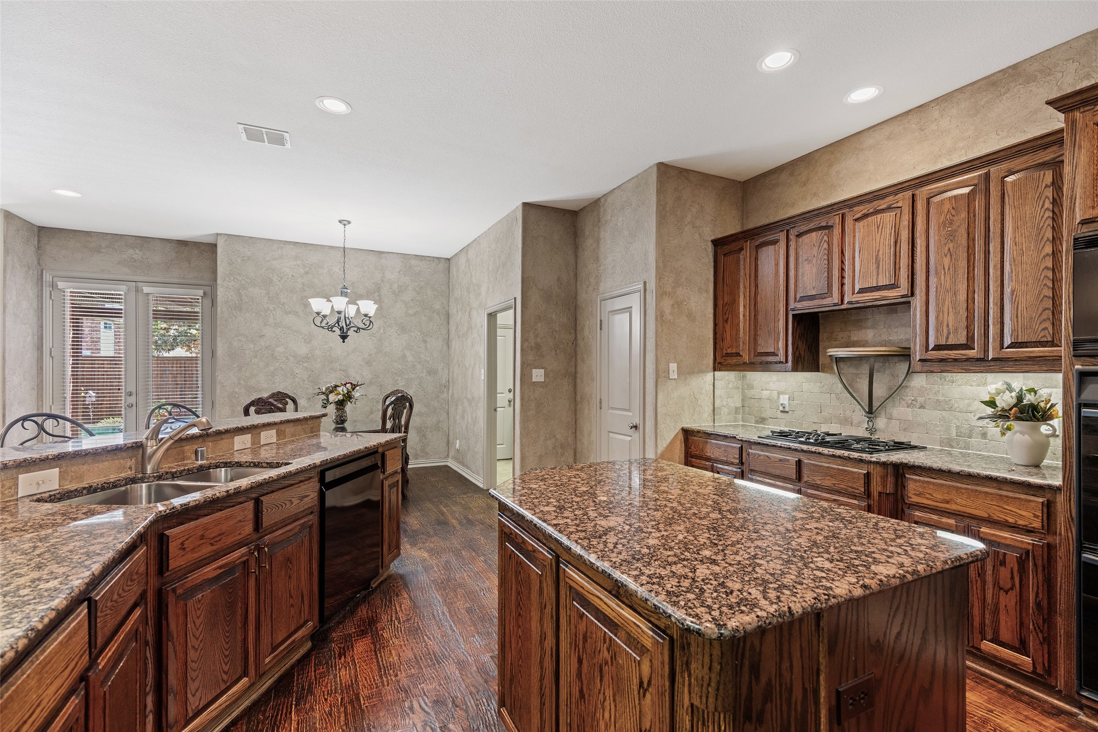 Kitchen with dark wood cabinets, granite counters, and a large island beside a dining area.