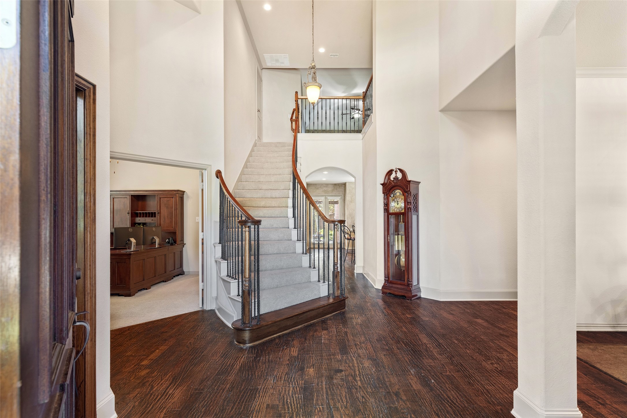 Two-story foyer with a curved staircase, dark hardwood floors, and a grandfather clock.