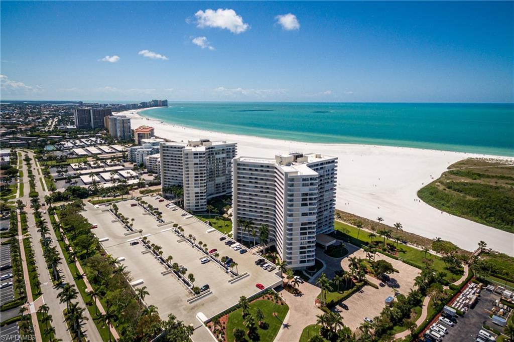 Beachfront condominium towers beside a long white-sand beach and turquoise Gulf water.