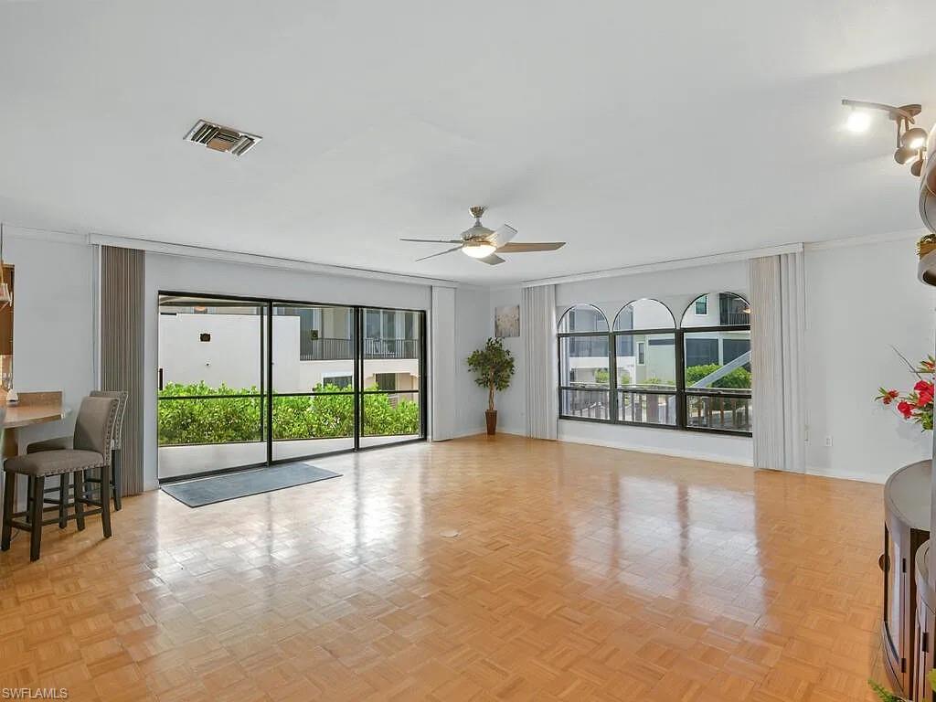 Living room with parquet floors, sliding glass doors, and arched windows overlooking greenery.
