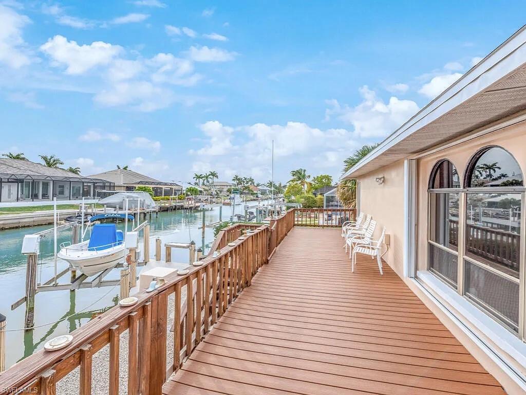 Waterfront deck with white chairs overlooking a canal and docked boat.