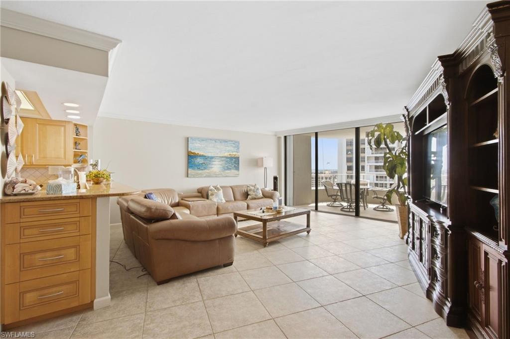 Condo living room with a tan sectional, kitchen breakfast bar, and balcony doors overlooking water.