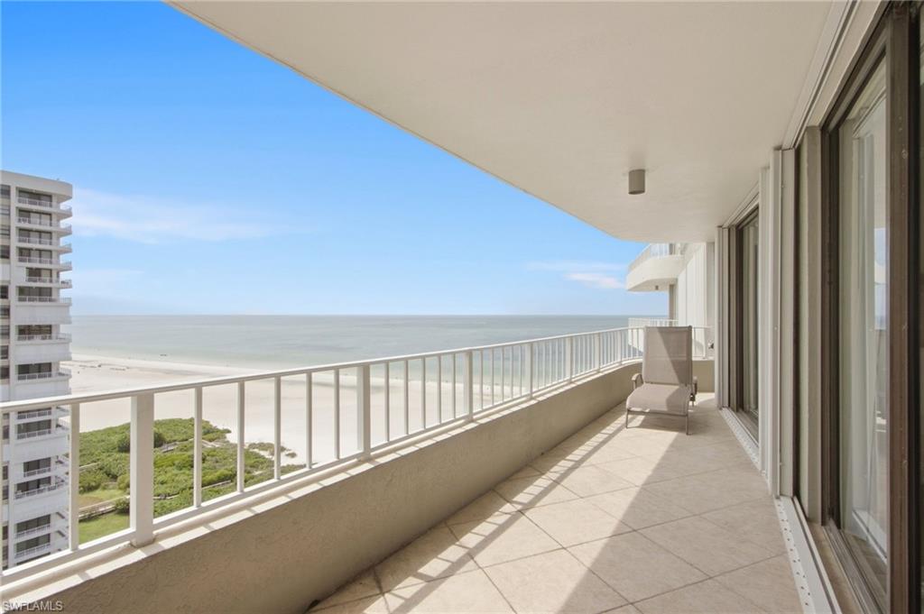 Condominium balcony overlooking the beach and ocean, with tiled flooring and a lounge chair.