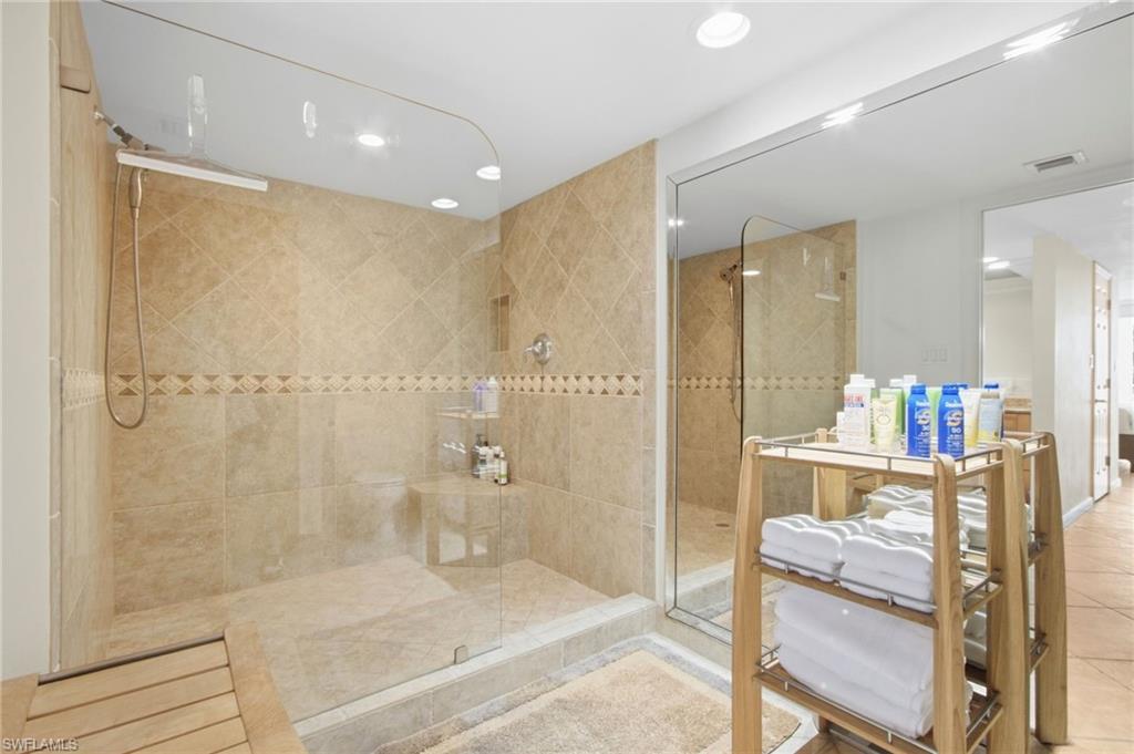 Bathroom with a glass-enclosed tiled walk-in shower, built-in bench, and towel cart.