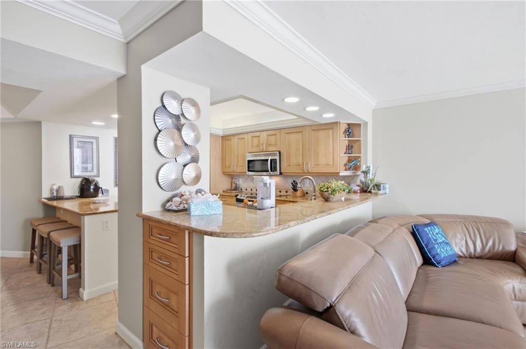 Condo kitchen with granite breakfast bar and light wood cabinets beside a beige leather sectional.