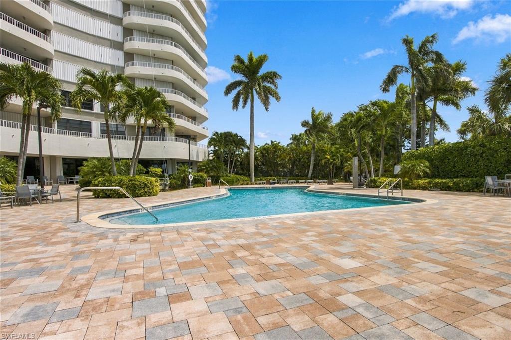 Condominium pool with a curved building, palm trees, and a spacious paved deck.