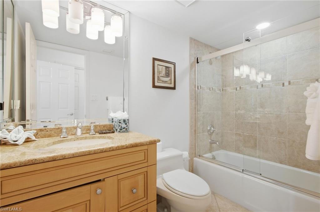 Bathroom with a wood vanity, tan stone countertop, and glass-enclosed tub and shower.