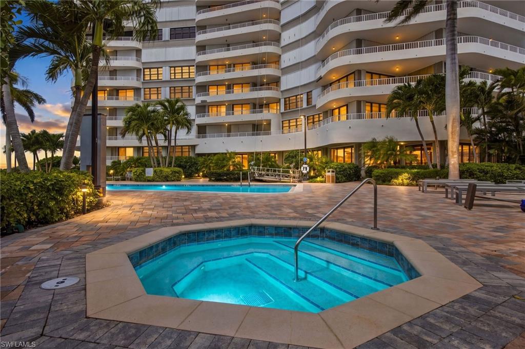 Condominium pool deck at dusk, with a raised spa, swimming pool, palm trees, and curved balconies.