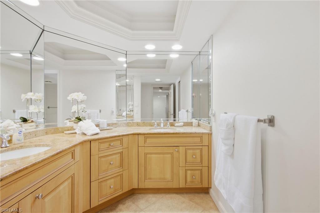 Bathroom with curved stone countertop, light wood cabinets, mirrored walls, and white orchids.