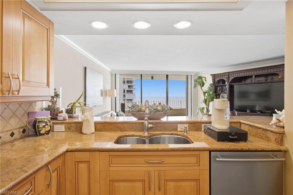 Kitchen with granite counters and wood cabinetry, looking through the living area toward a water view.