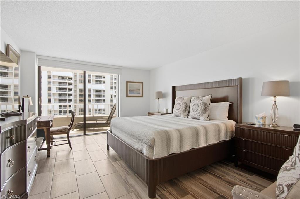 Furnished condominium bedroom with a dark wood bed and sliding doors to a balcony overlooking neighboring towers.