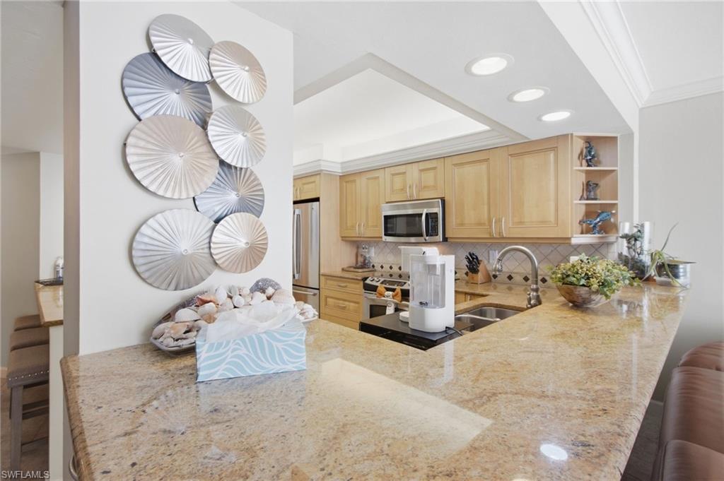 Kitchen with light wood cabinets, stainless appliances, and a large granite peninsula with bar seating.