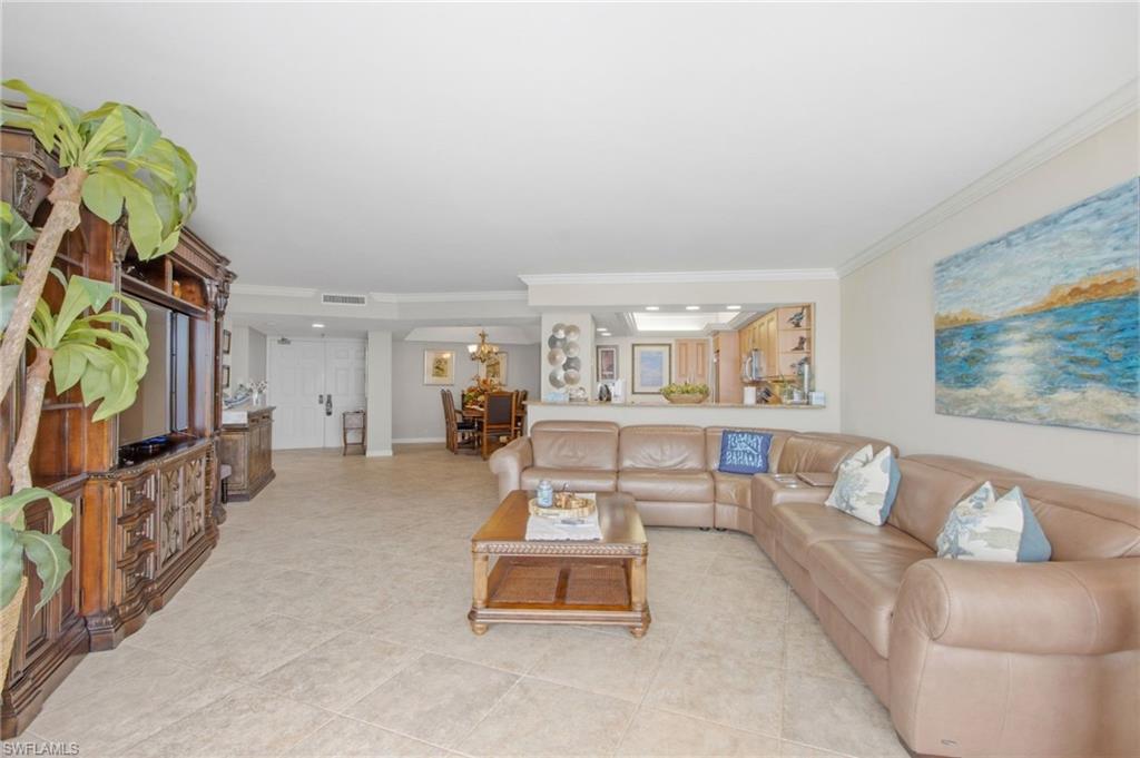 Condo living room with a beige sectional, tiled floors, and an open dining and kitchen area.