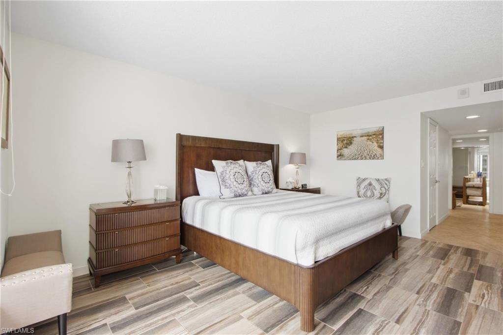 Furnished bedroom with a dark wood bed, white bedding, matching dresser, and wood-look tile floor.