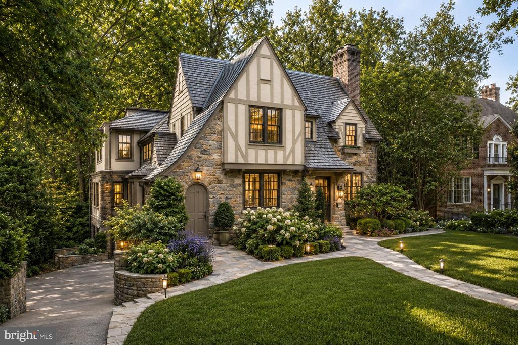 Tudor-style stone home with illuminated windows, a curved walkway, and landscaped front lawn.