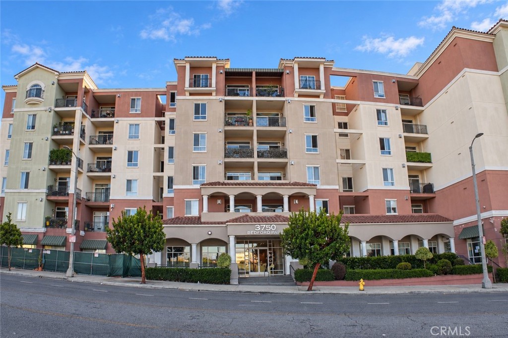 Multi-story condominium building with balconies and a landscaped street-level entrance.
