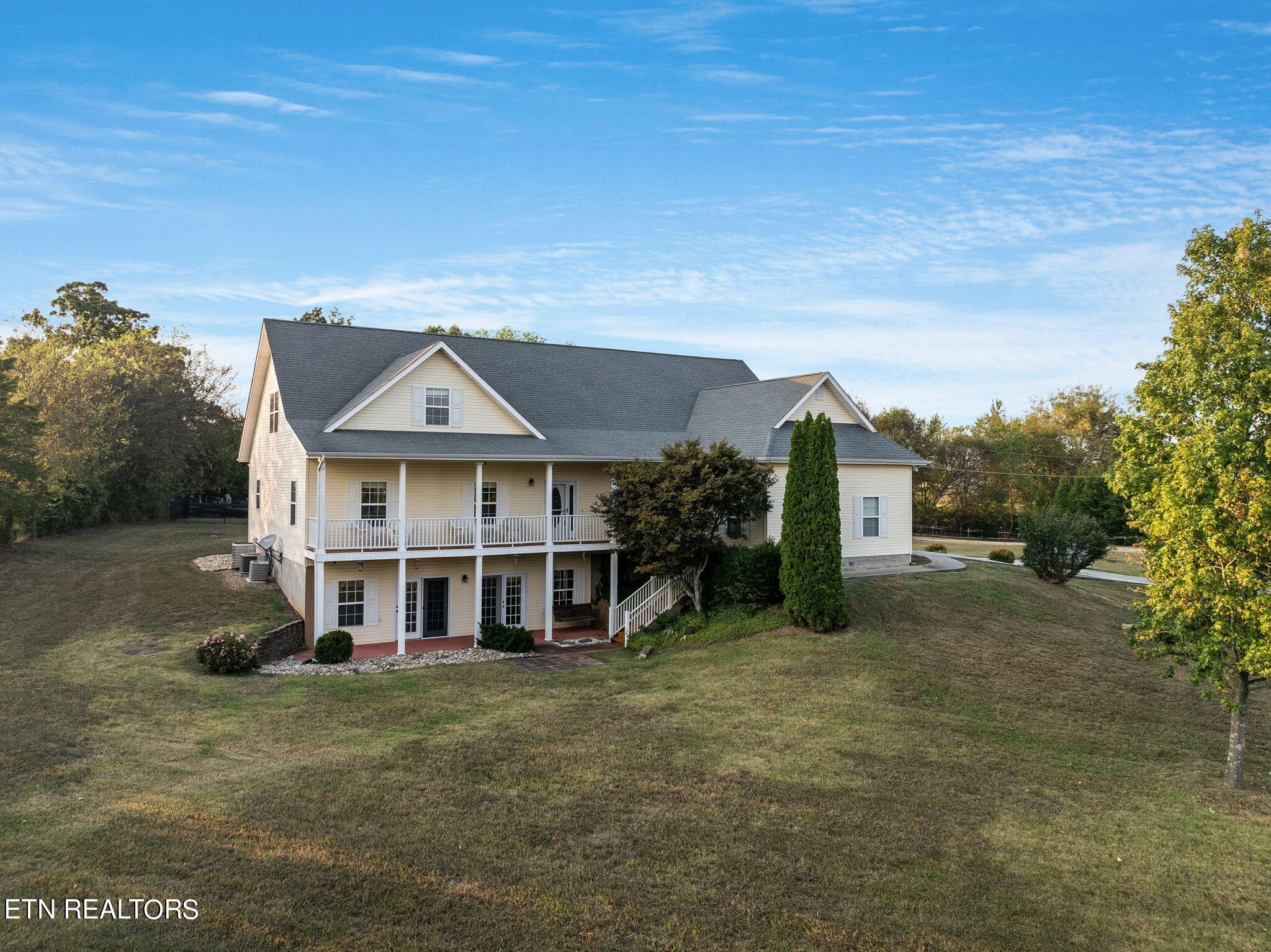Two-story cream house with a covered porch, surrounded by a broad lawn and mature trees.