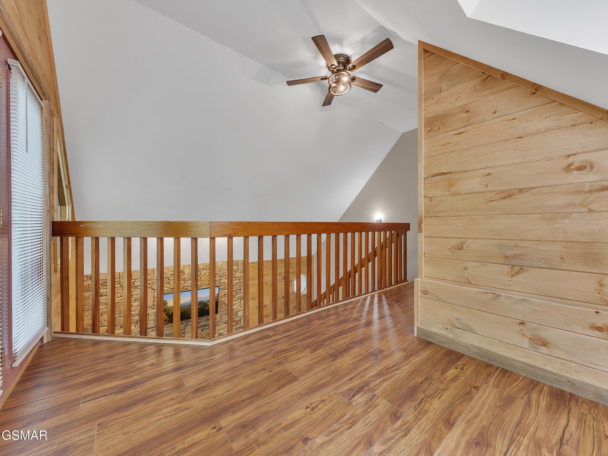 Upstairs loft landing with wood flooring, a wooden stair railing, vaulted ceiling and ceiling fan.