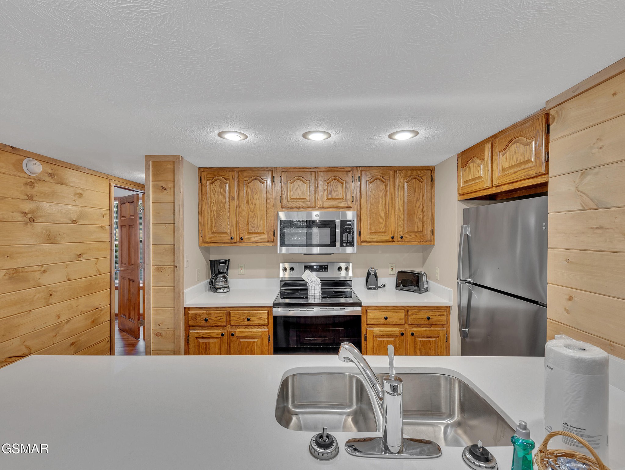 Kitchen with honey-colored wood cabinets, stainless steel appliances, and a double-basin sink.