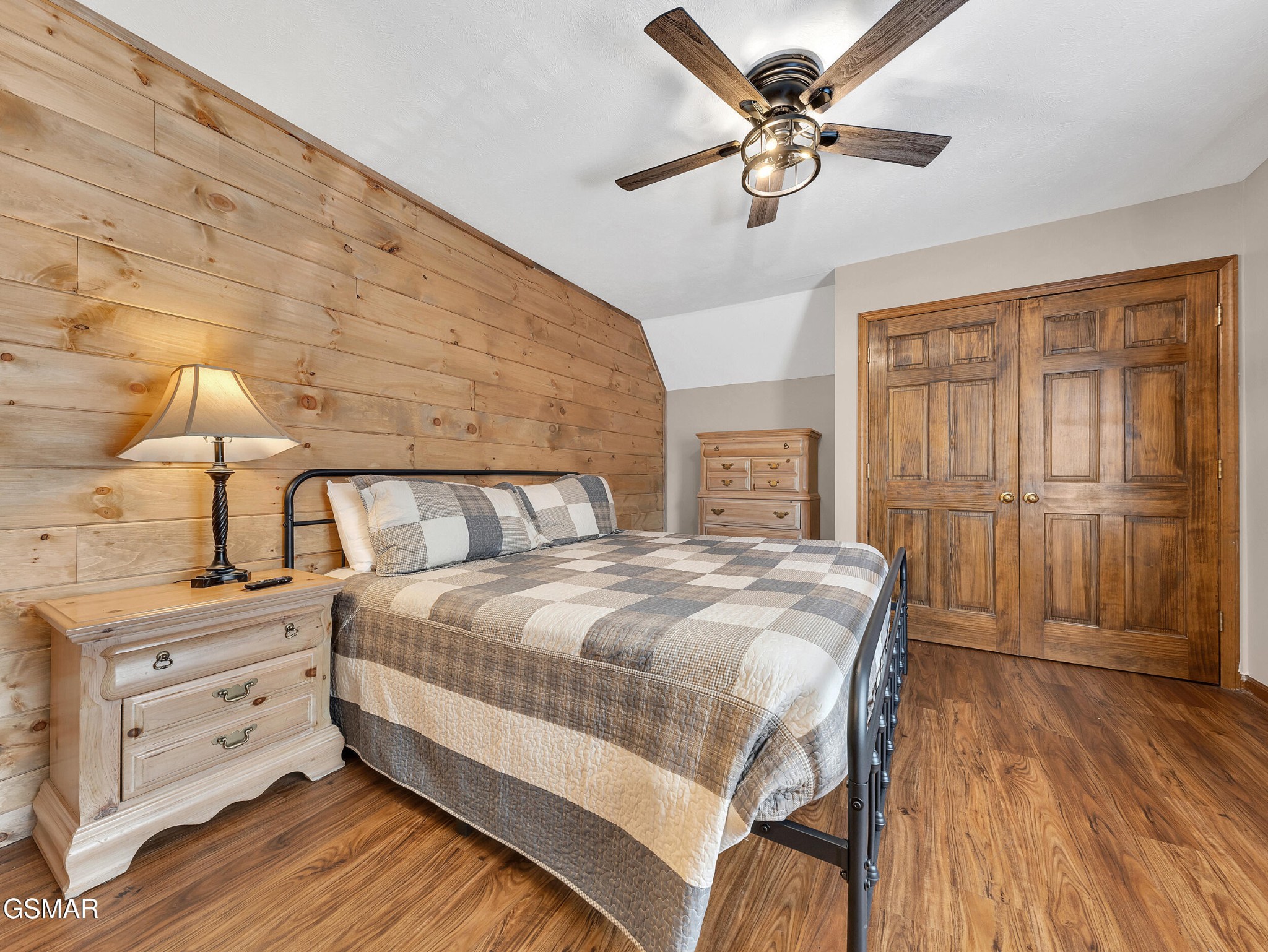 Bedroom with a patchwork quilt, wood-plank accent wall, and matching wooden double doors.
