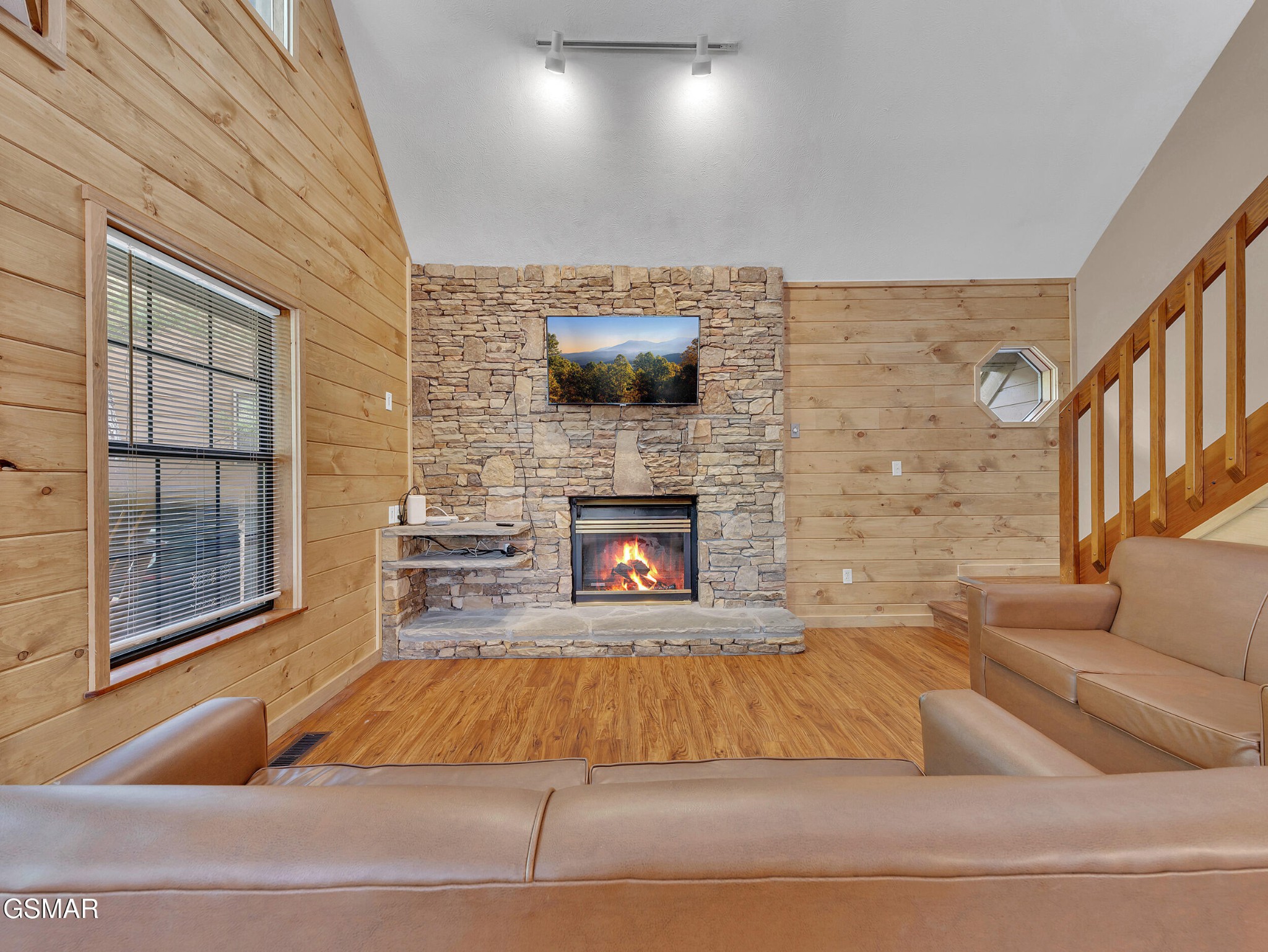 Cabin living room with a lit stone fireplace, wood-paneled walls, and leather seating.