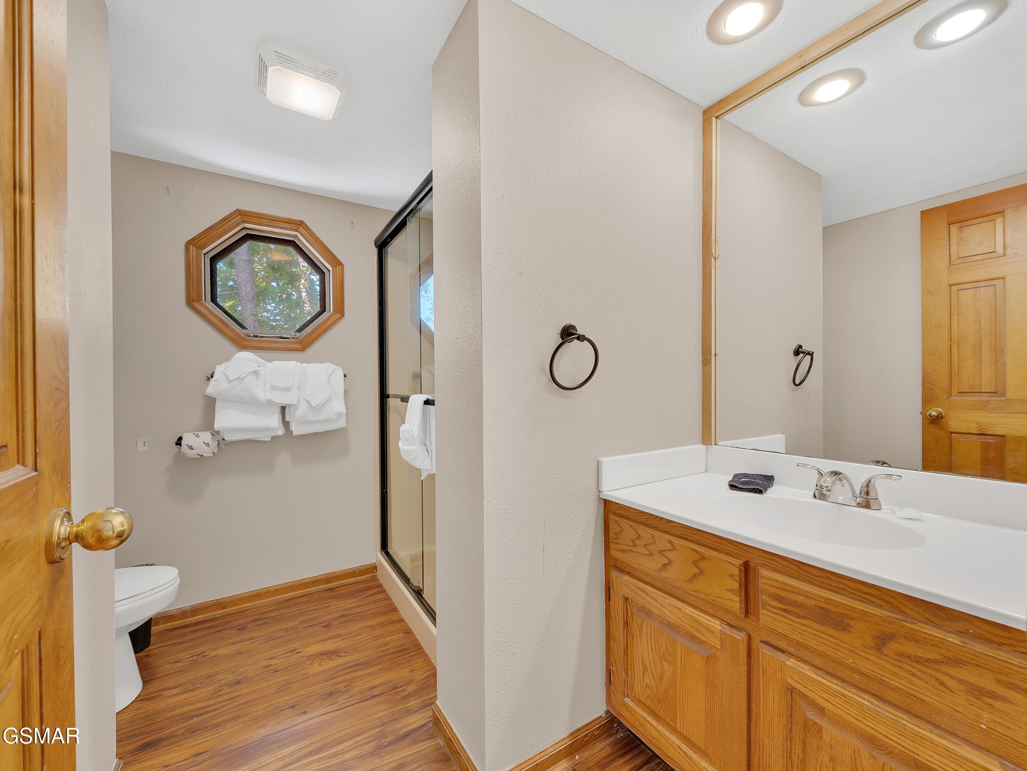 Bathroom with a wood vanity, glass shower, and octagonal window.