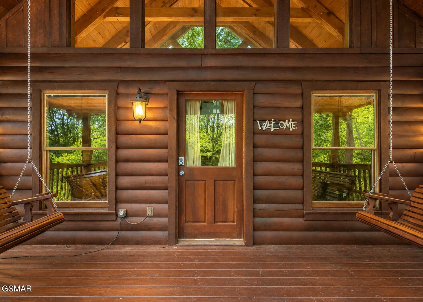 Log cabin porch with a central wooden door and hanging swings on both sides.