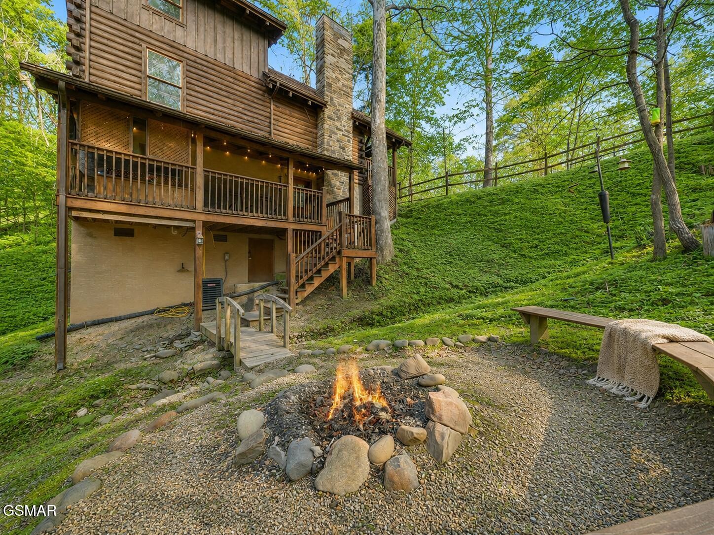 Wooded log cabin with covered porches and a stone-ringed fire pit.