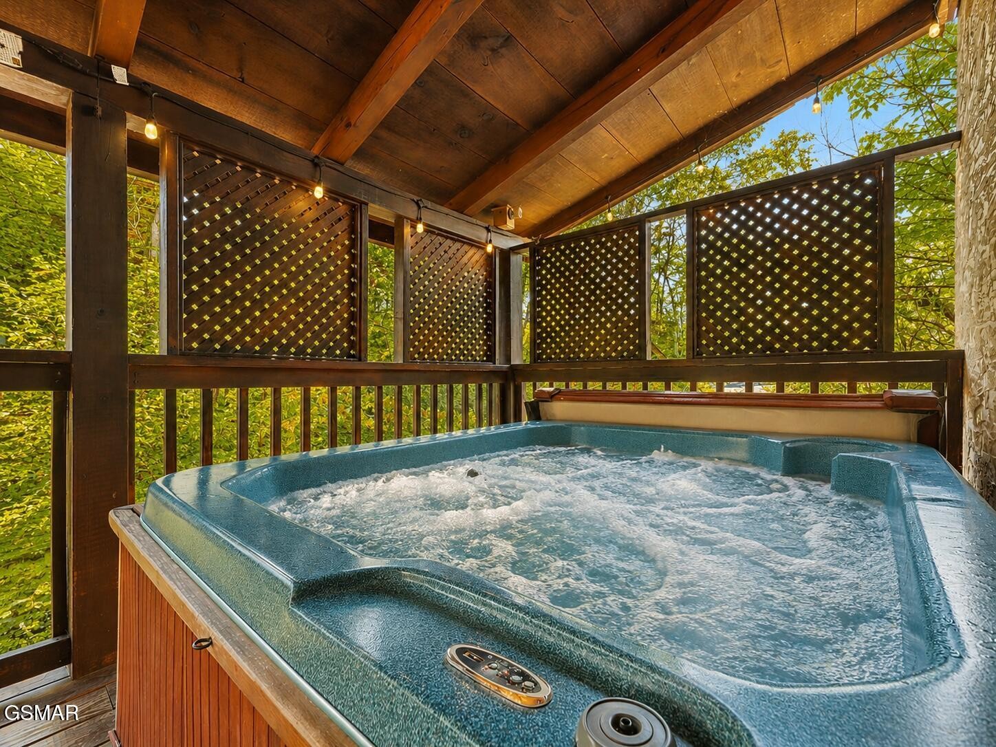 Hot tub on a covered wooden deck with lattice screens and leafy wooded surroundings.
