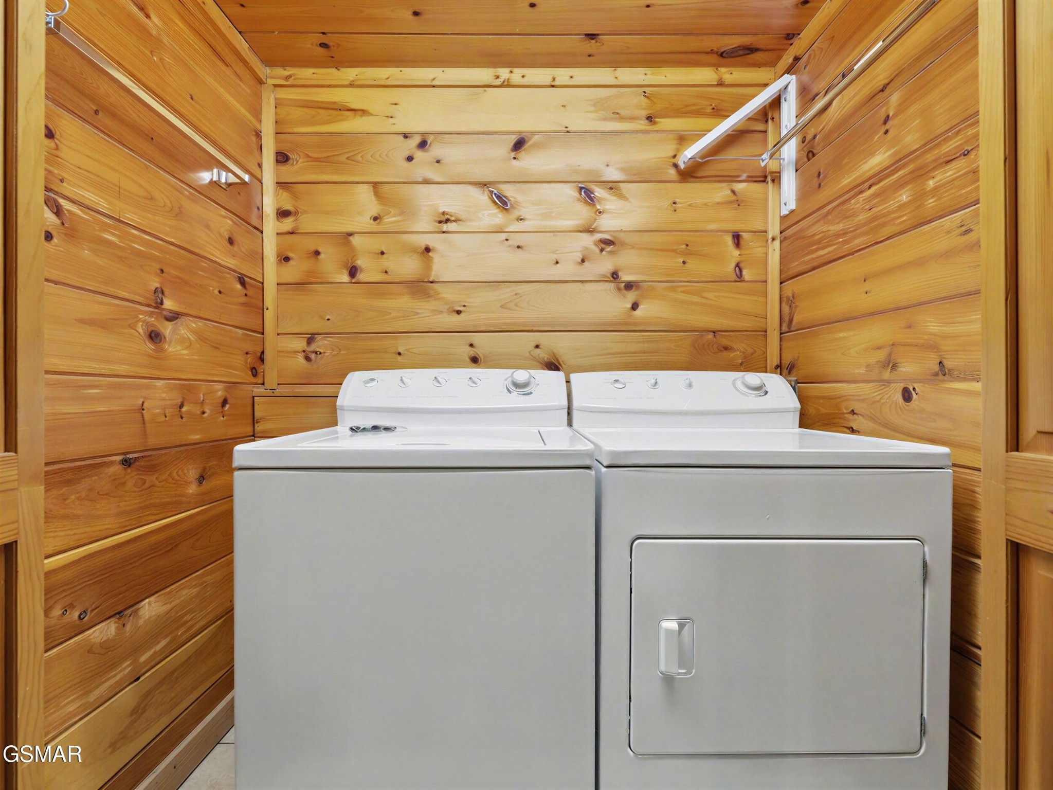 Laundry room with washer and dryer surrounded by warm knotty-pine walls.
