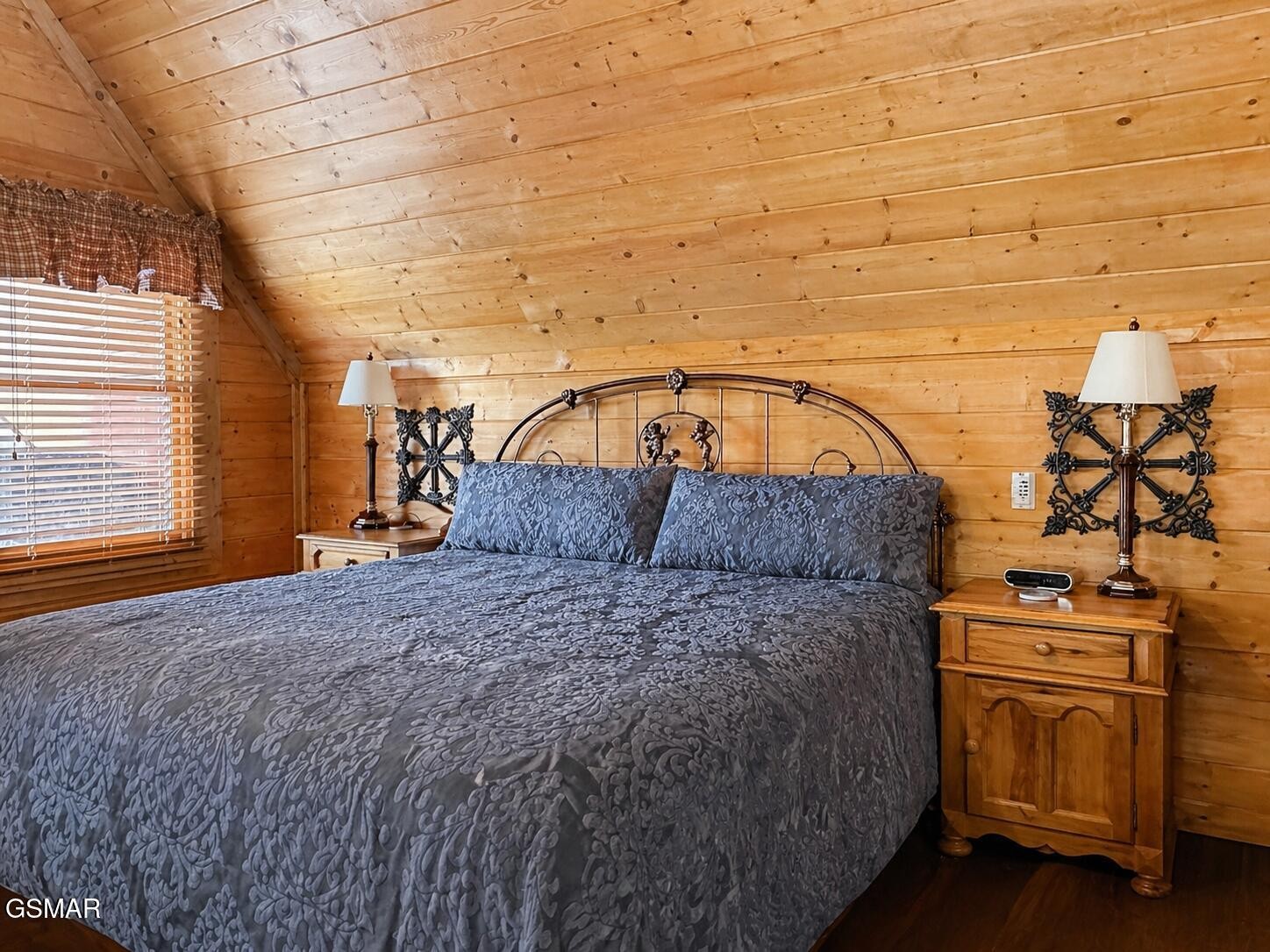 Cabin bedroom with a large bed, ornate metal headboard, and warm wood-plank walls and ceiling.