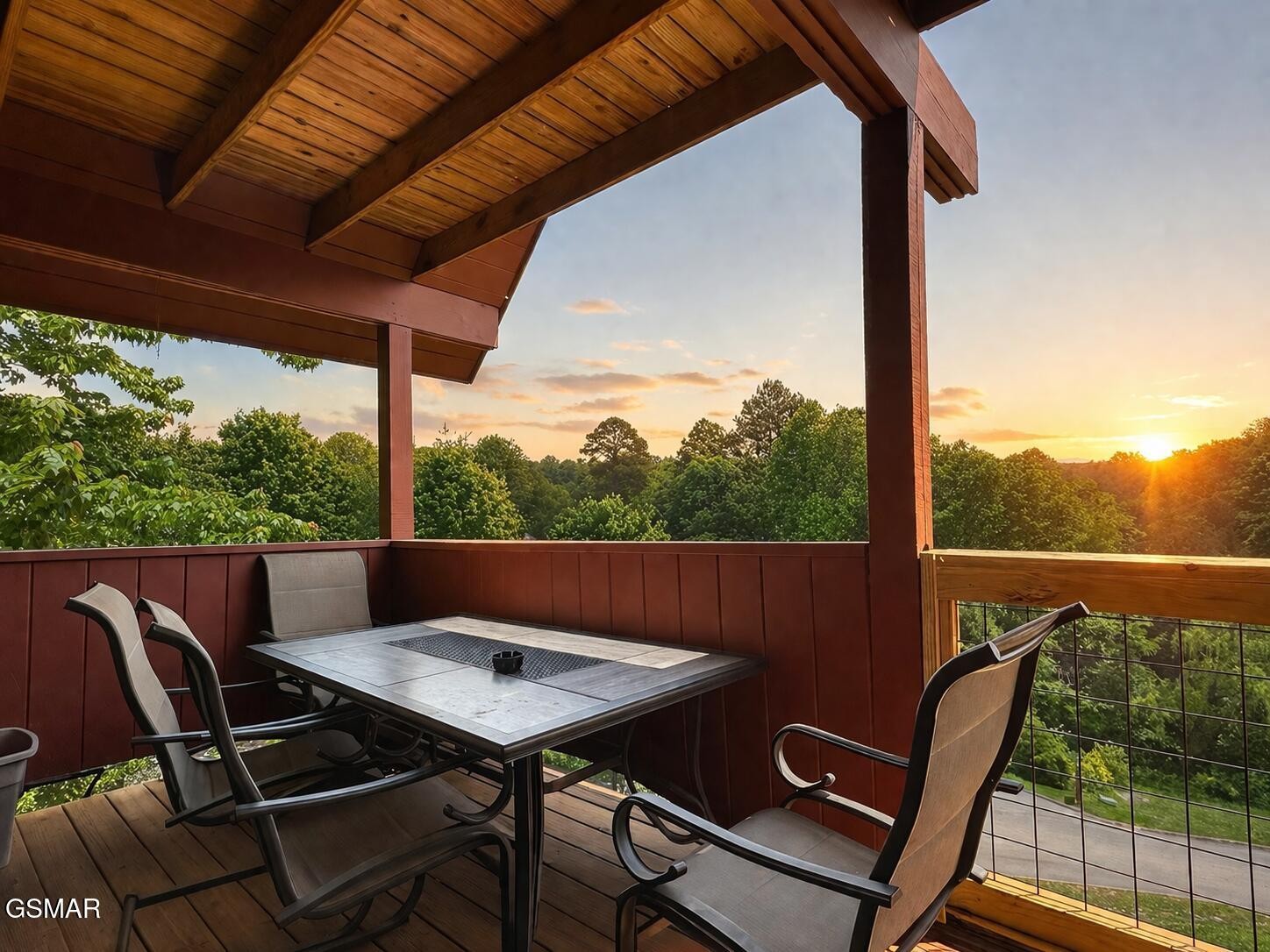 Covered deck with an outdoor dining set overlooking trees at sunset.
