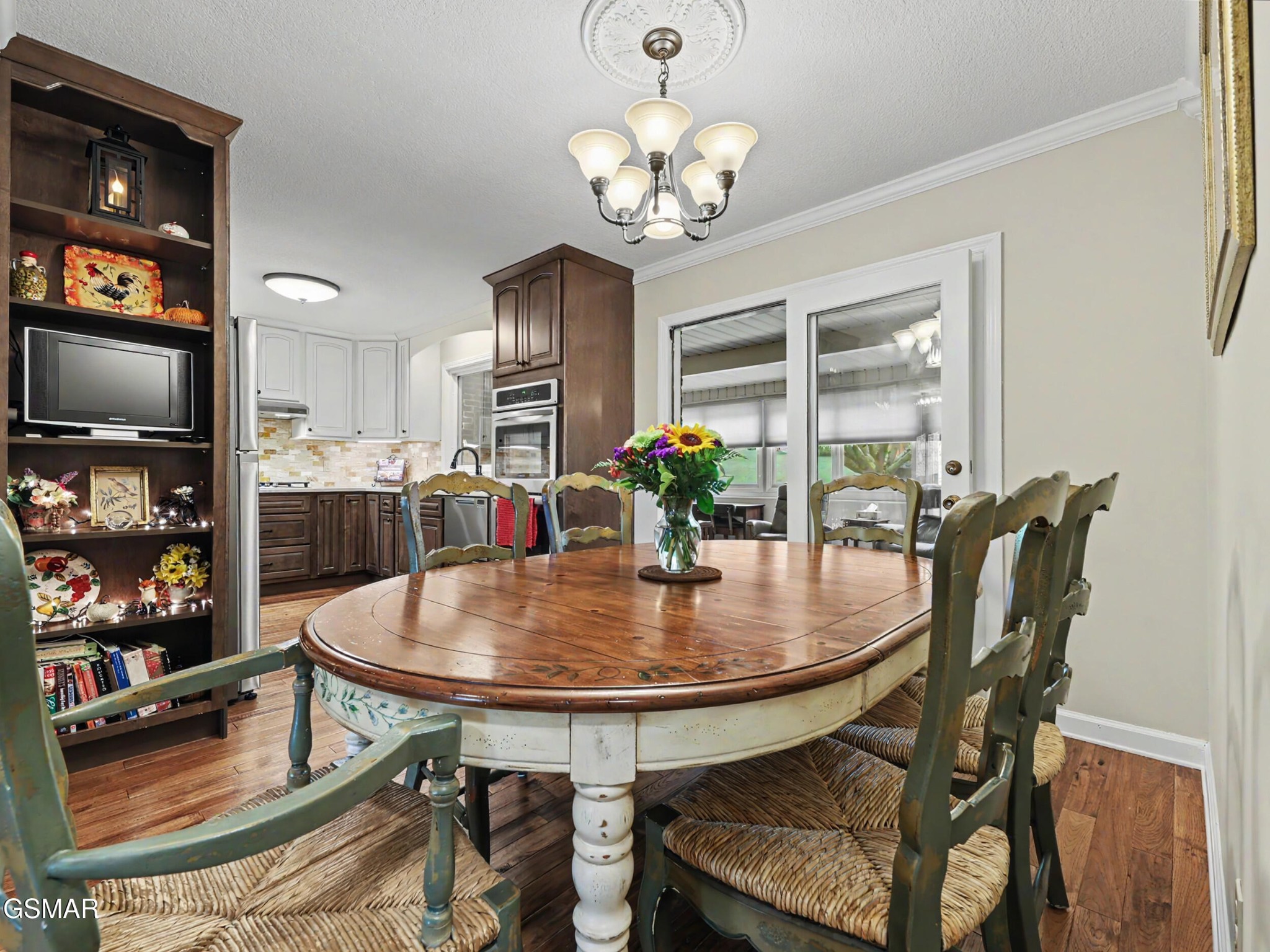 Dining room with a round wood table, woven-seat chairs, and a flower centerpiece beside the kitchen.