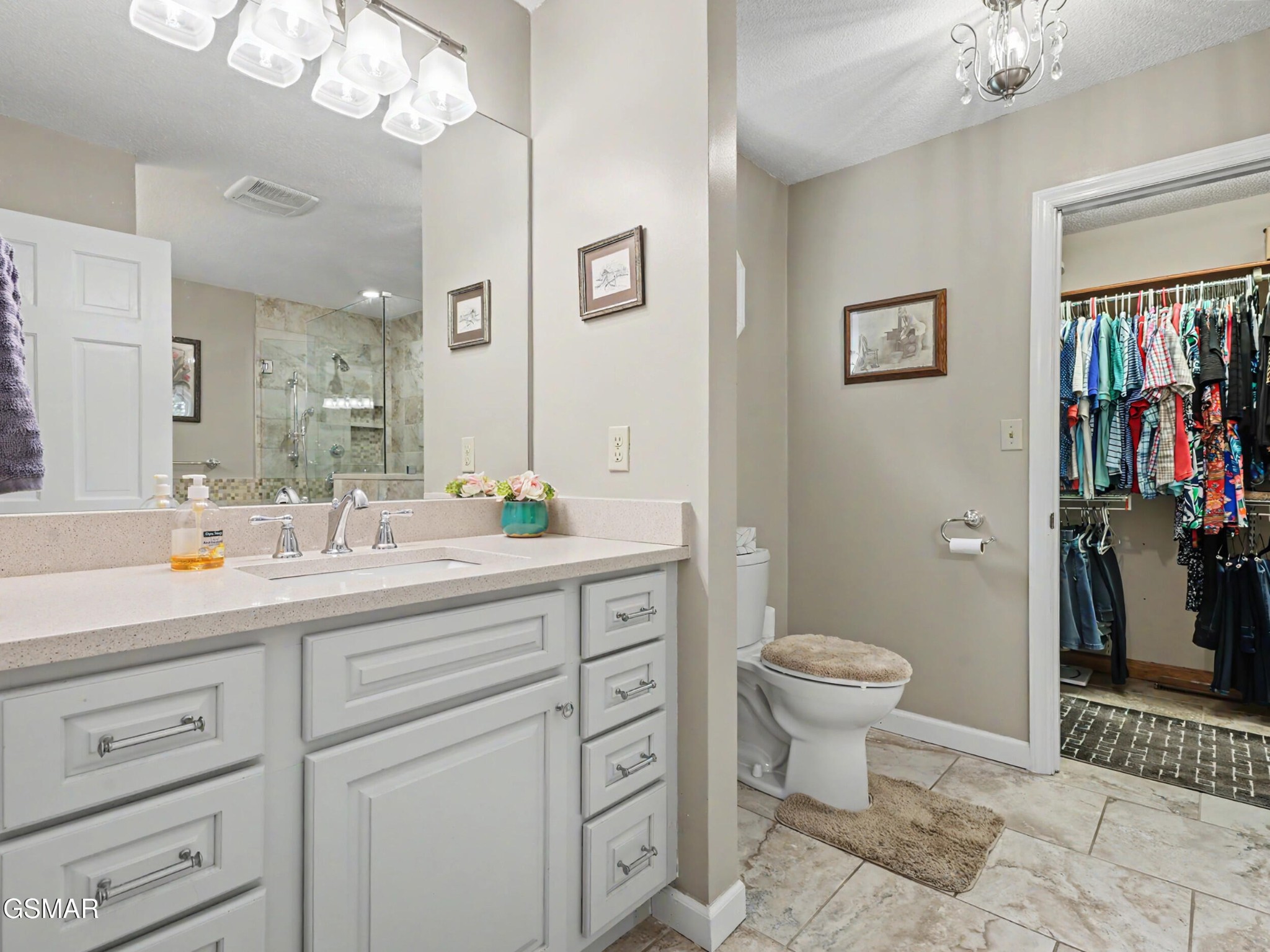 Bathroom with a white vanity, glass shower, toilet, and open walk-in closet.