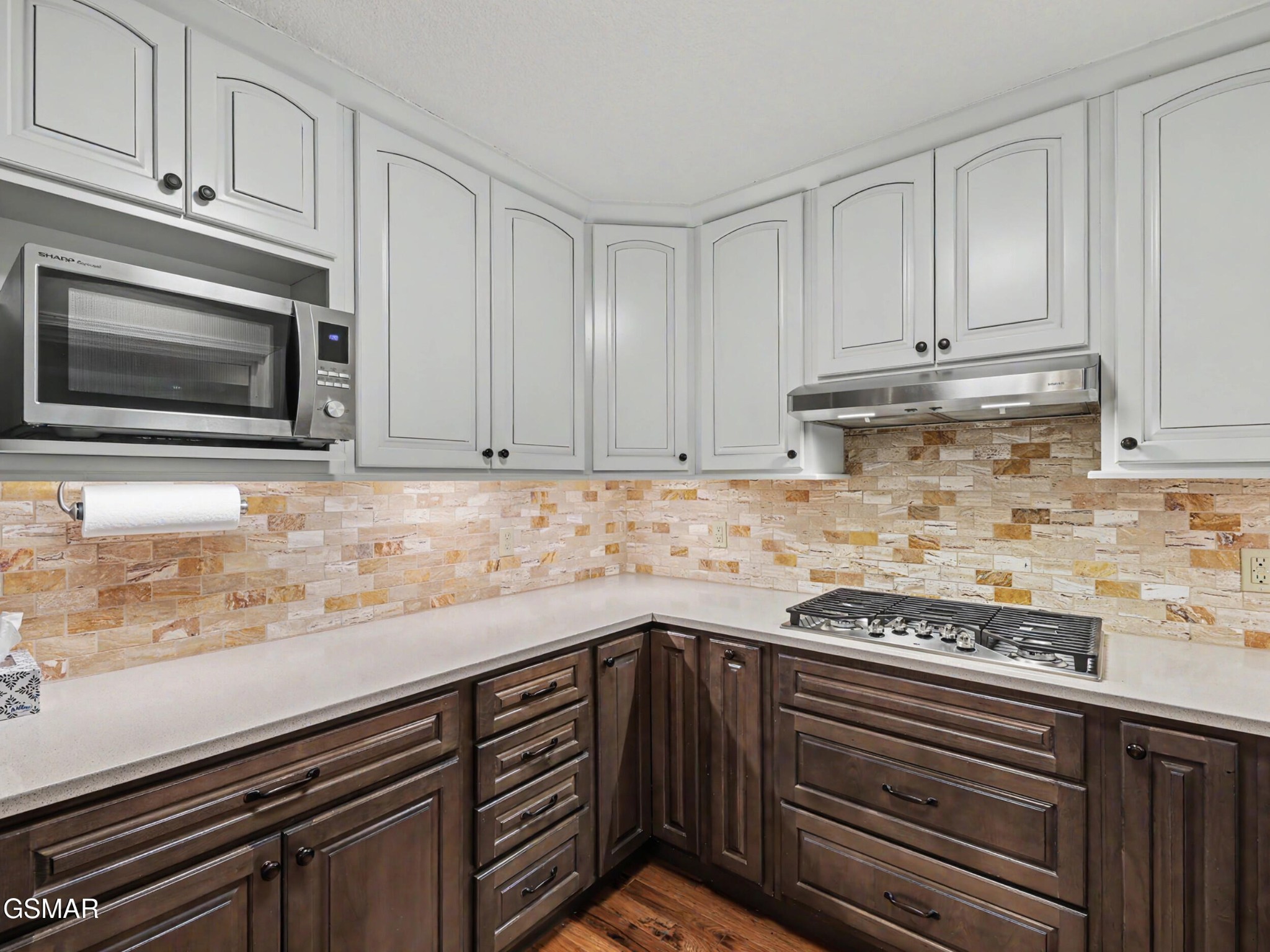 Kitchen with white upper cabinets, dark wood lower cabinets, and a tan stone-tile backsplash.