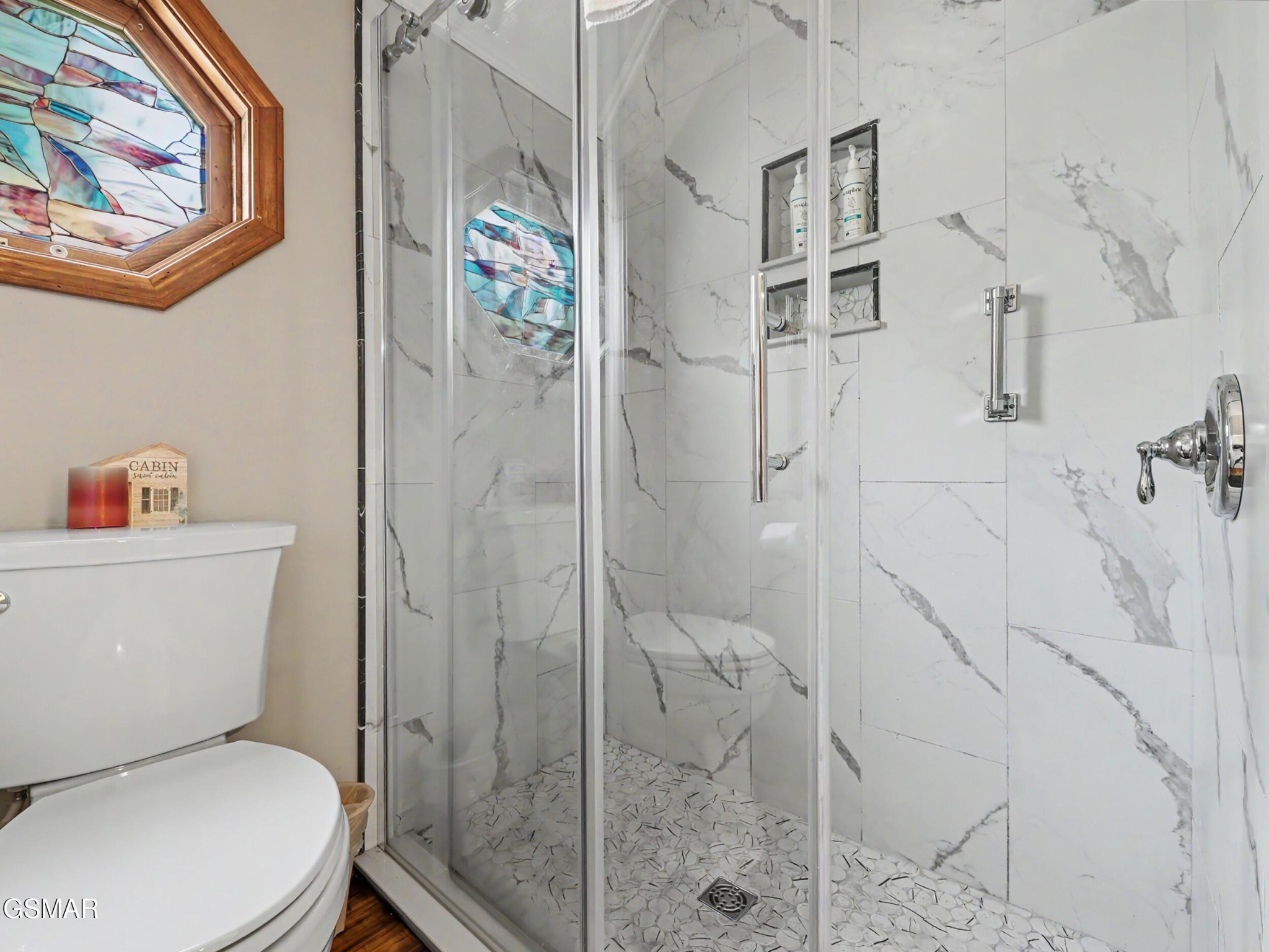 Bathroom with a glass-enclosed marble-look shower, mosaic floor, and stained-glass window.