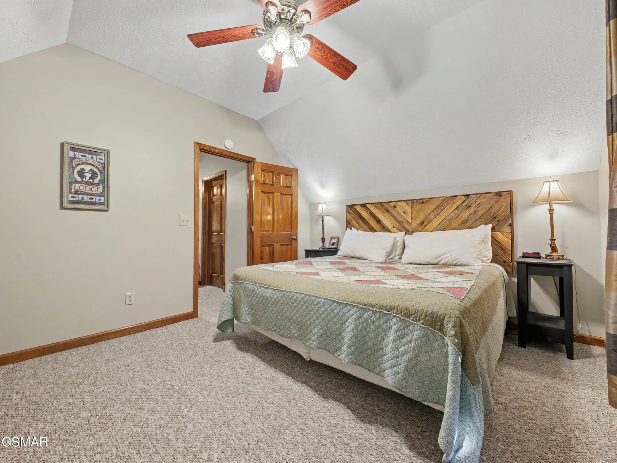Bedroom with a king bed, rustic geometric wood headboard, and vaulted ceiling with a ceiling fan.