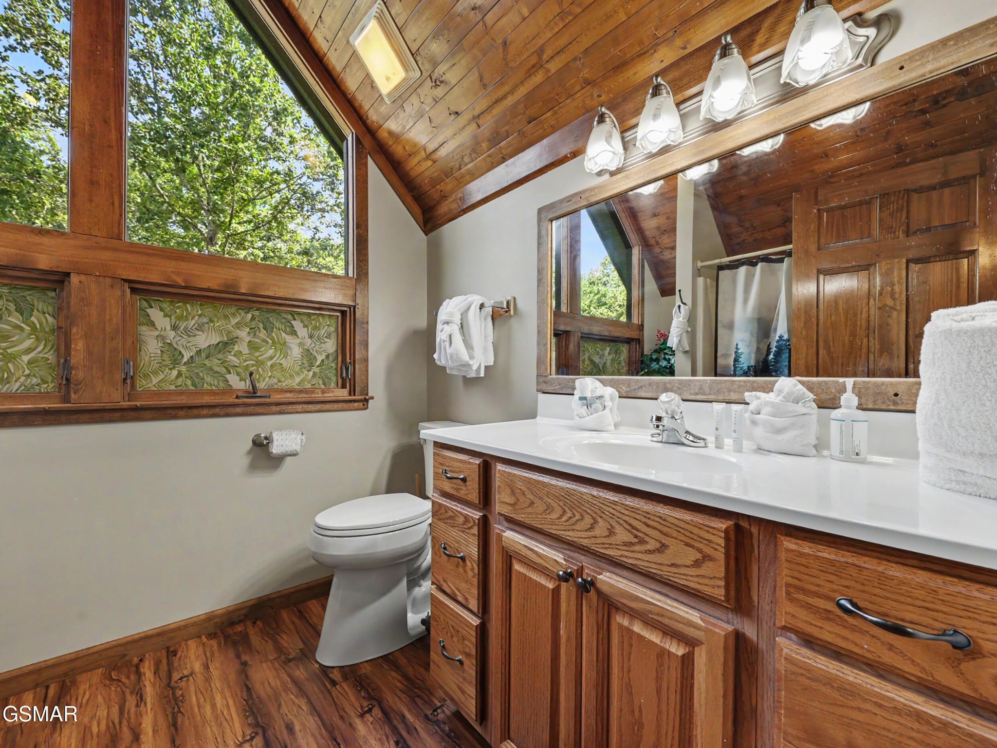 Cabin bathroom with a vaulted wood ceiling, large windows, and a wood vanity with white countertop.