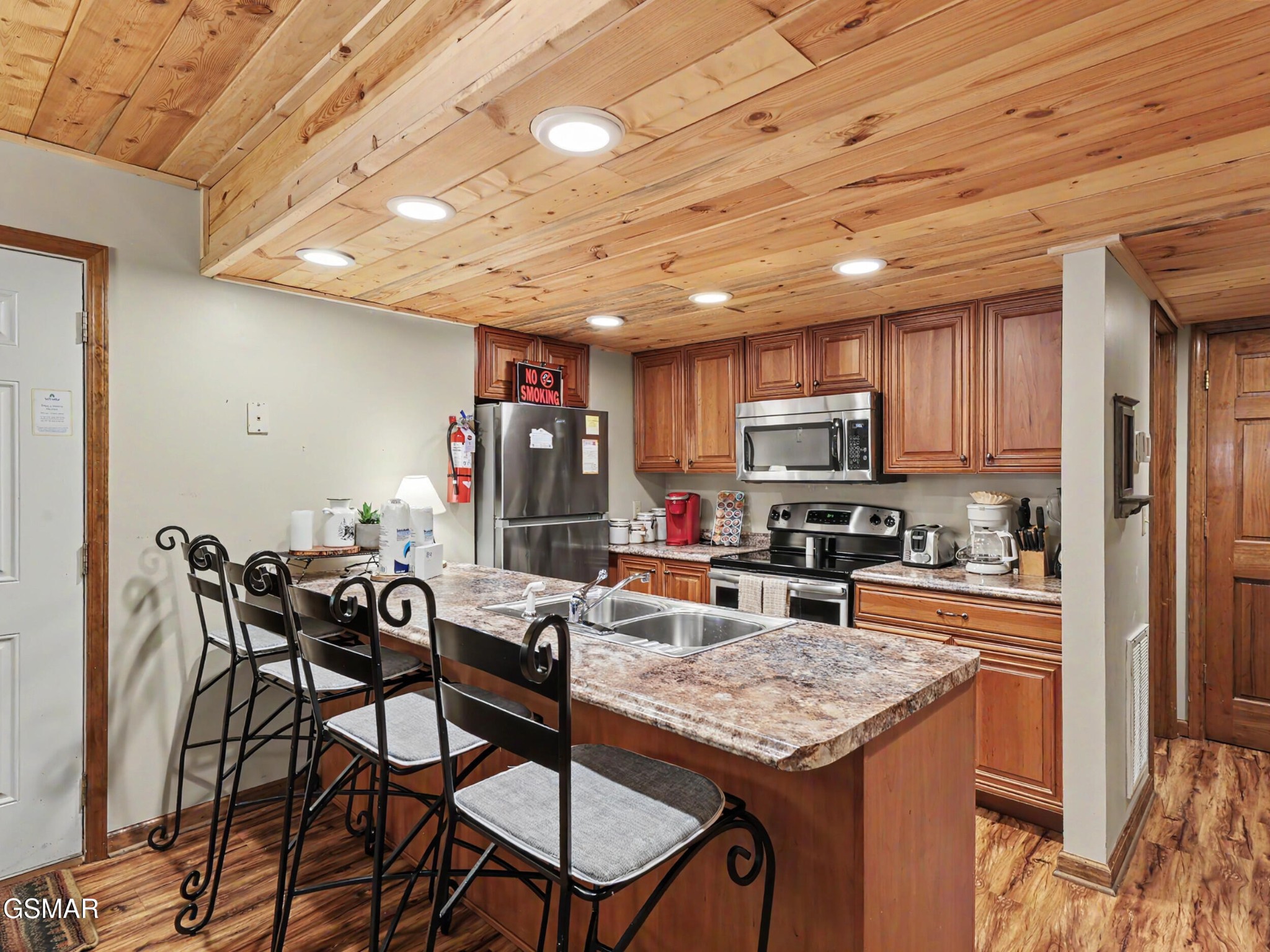 Kitchen with a granite island and bar seating beneath a distinctive natural wood plank ceiling.